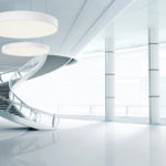 A stylish white office space with a spiral staircase and 2 large round pendant lights.